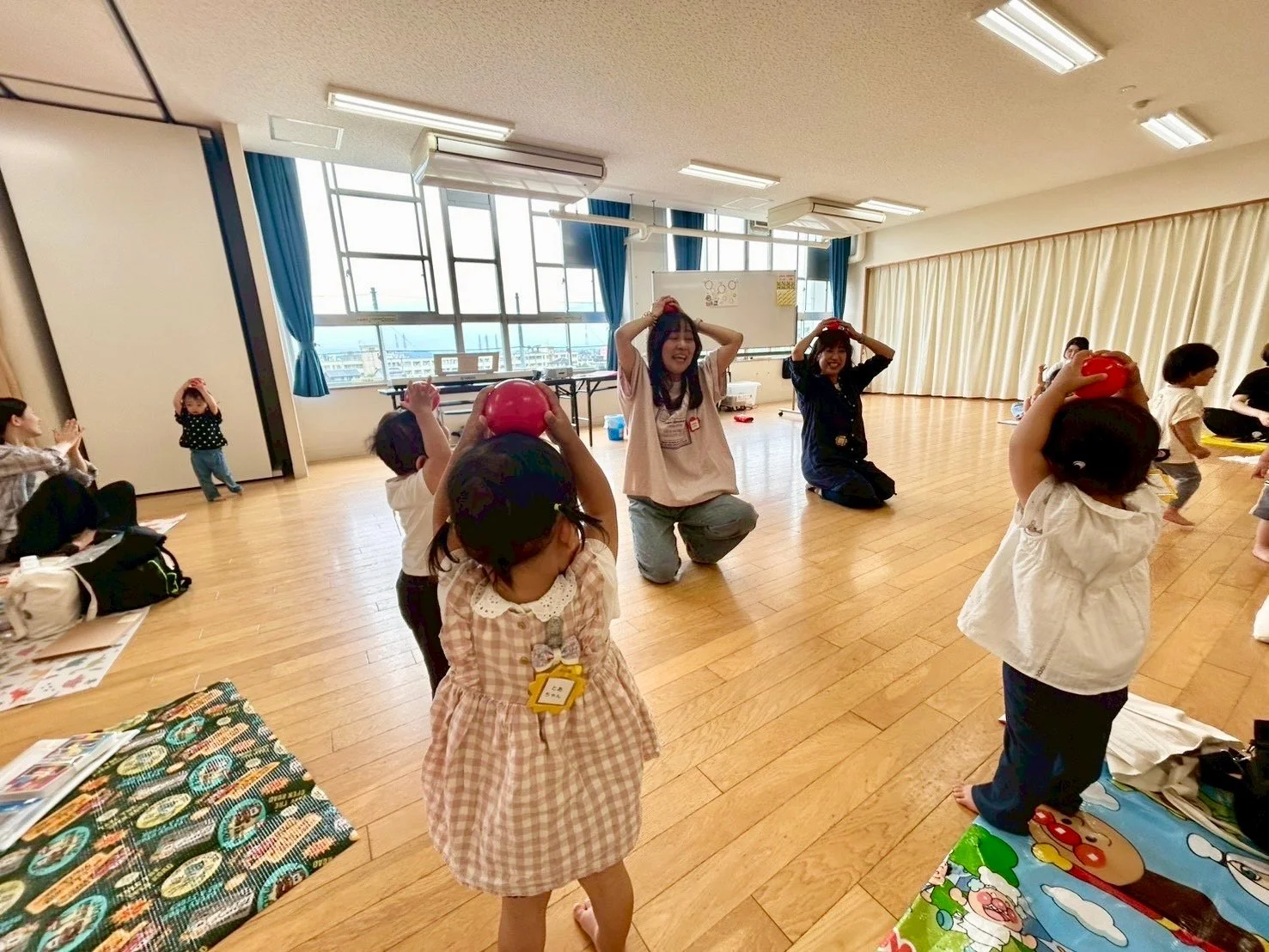 親子が床の上で円になり、タンバリンやスカーフを使って音楽に合わせて体を動かしている様子
